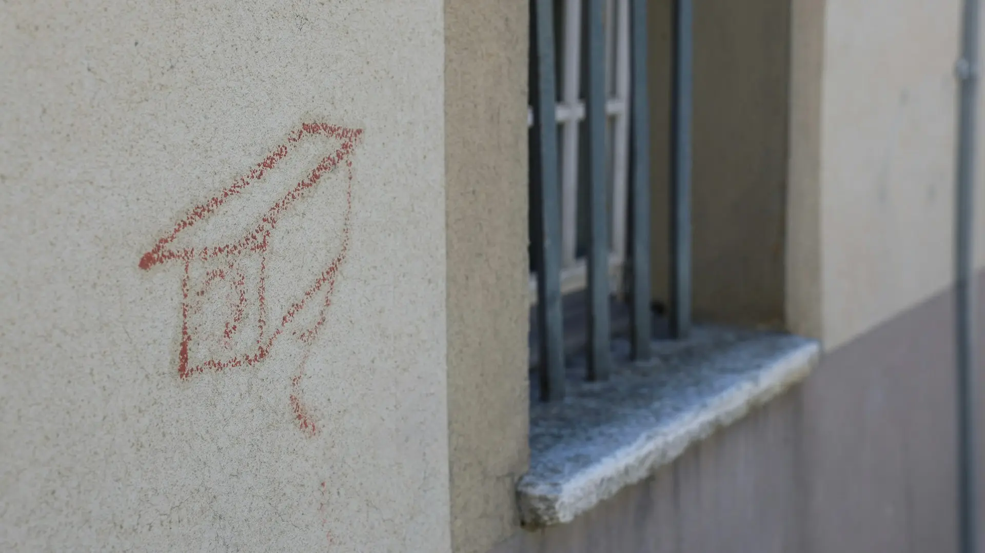 Red chalk drawing of a house on a wall.
